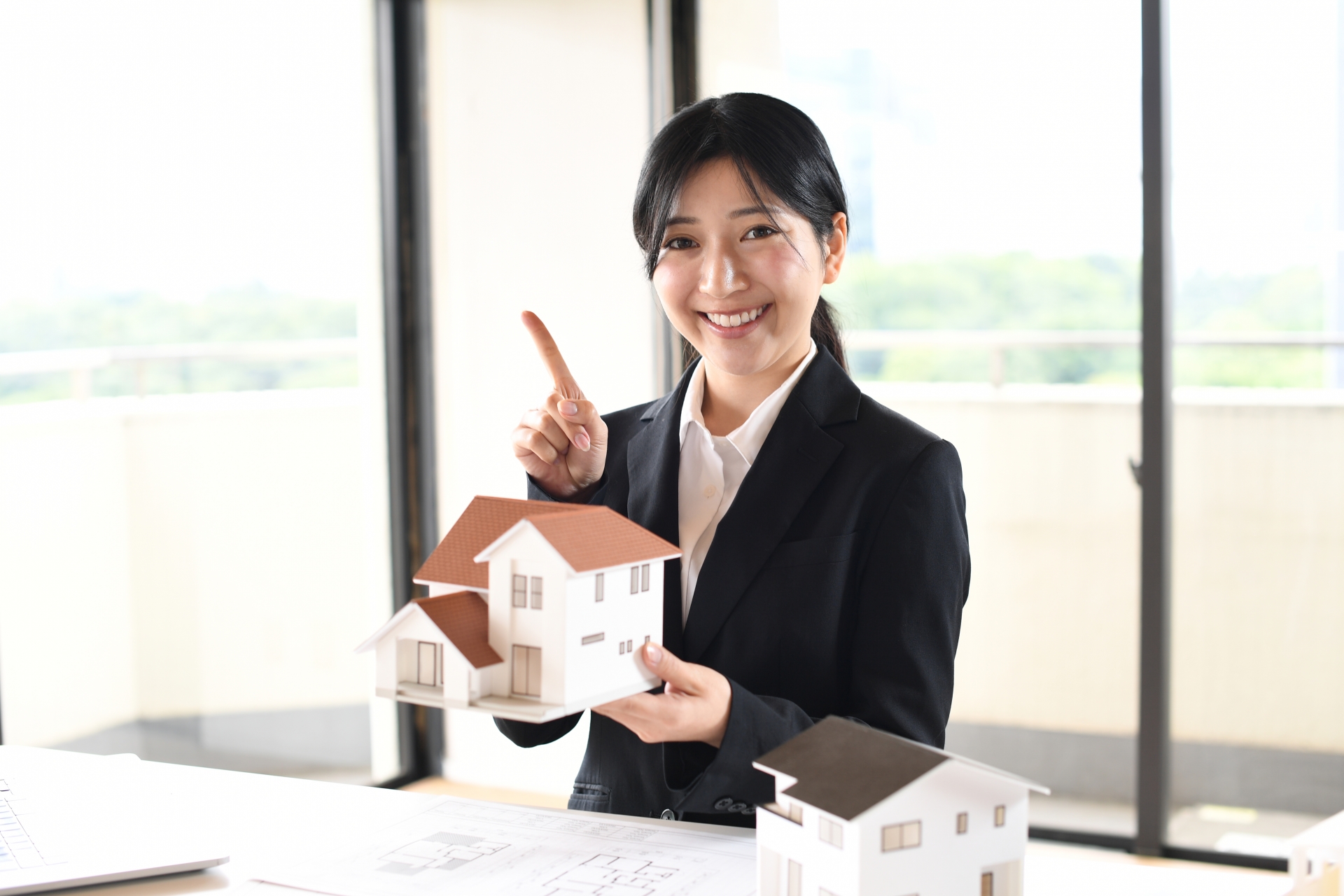 家の模型を持って人差し指を立てている女性