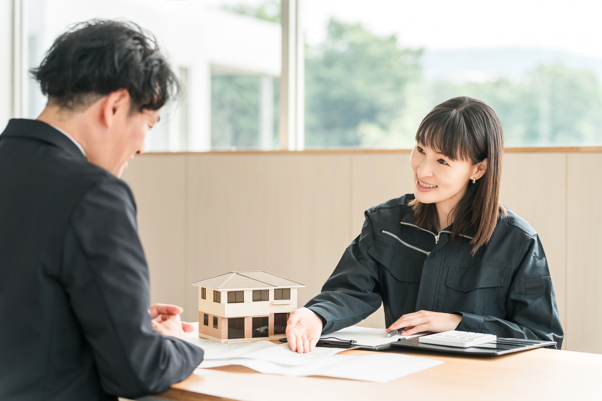 住宅模型を使って説明をする作業着の女性