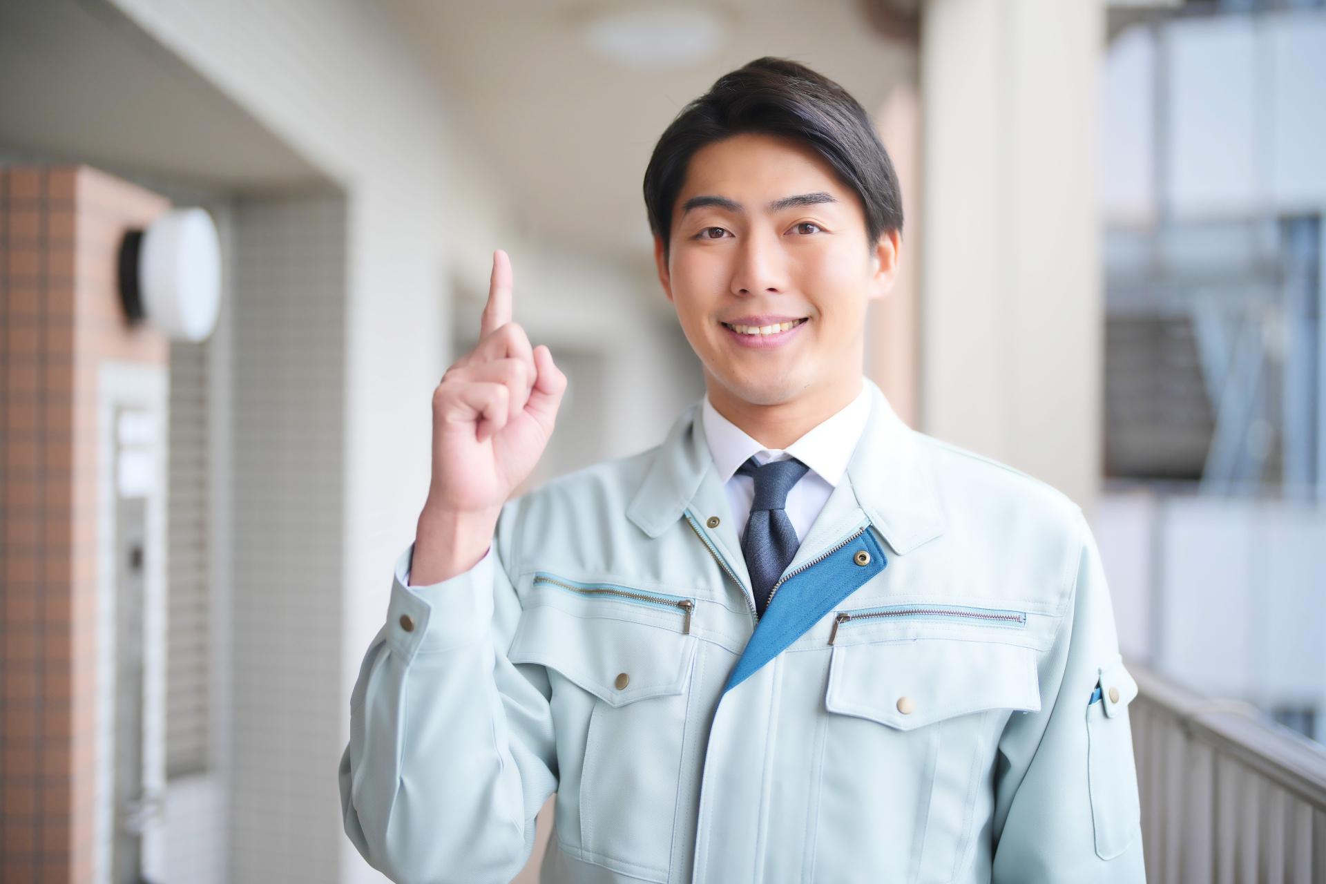 団地の廊下で指を1本立てる男性