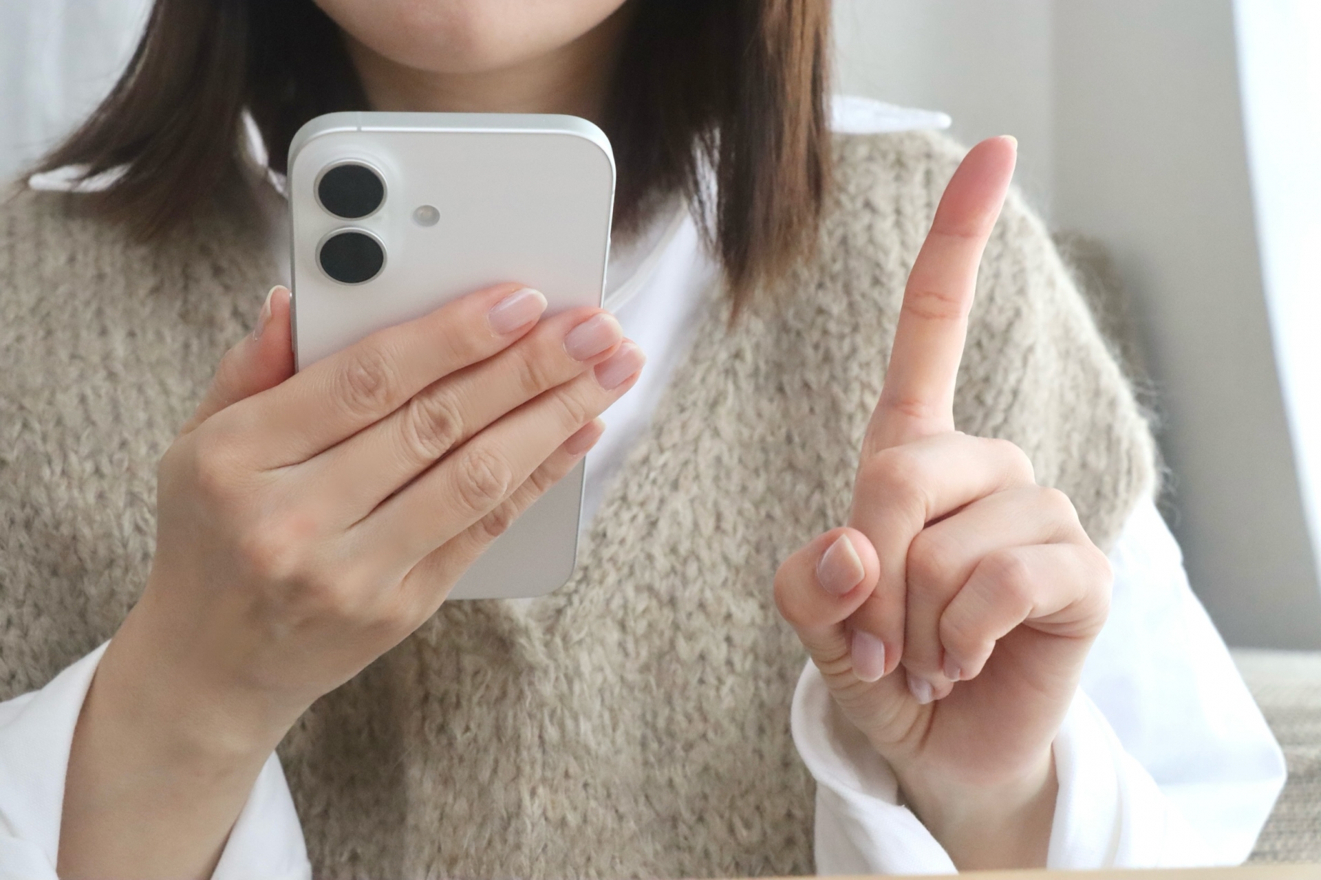 スマホを見て人差し指を立てている女性