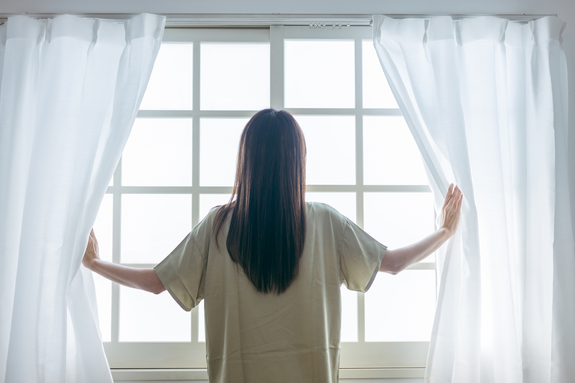 窓を開けるミドル世代の女性(起床)